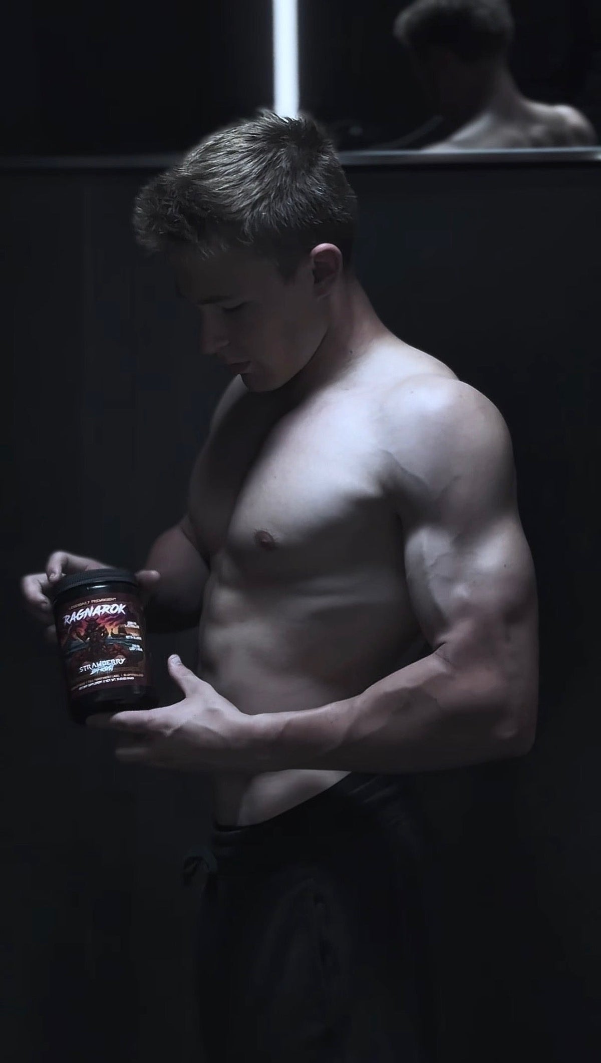 Man holding a tub of Ragnarok pre-workout in front of a gym mirror