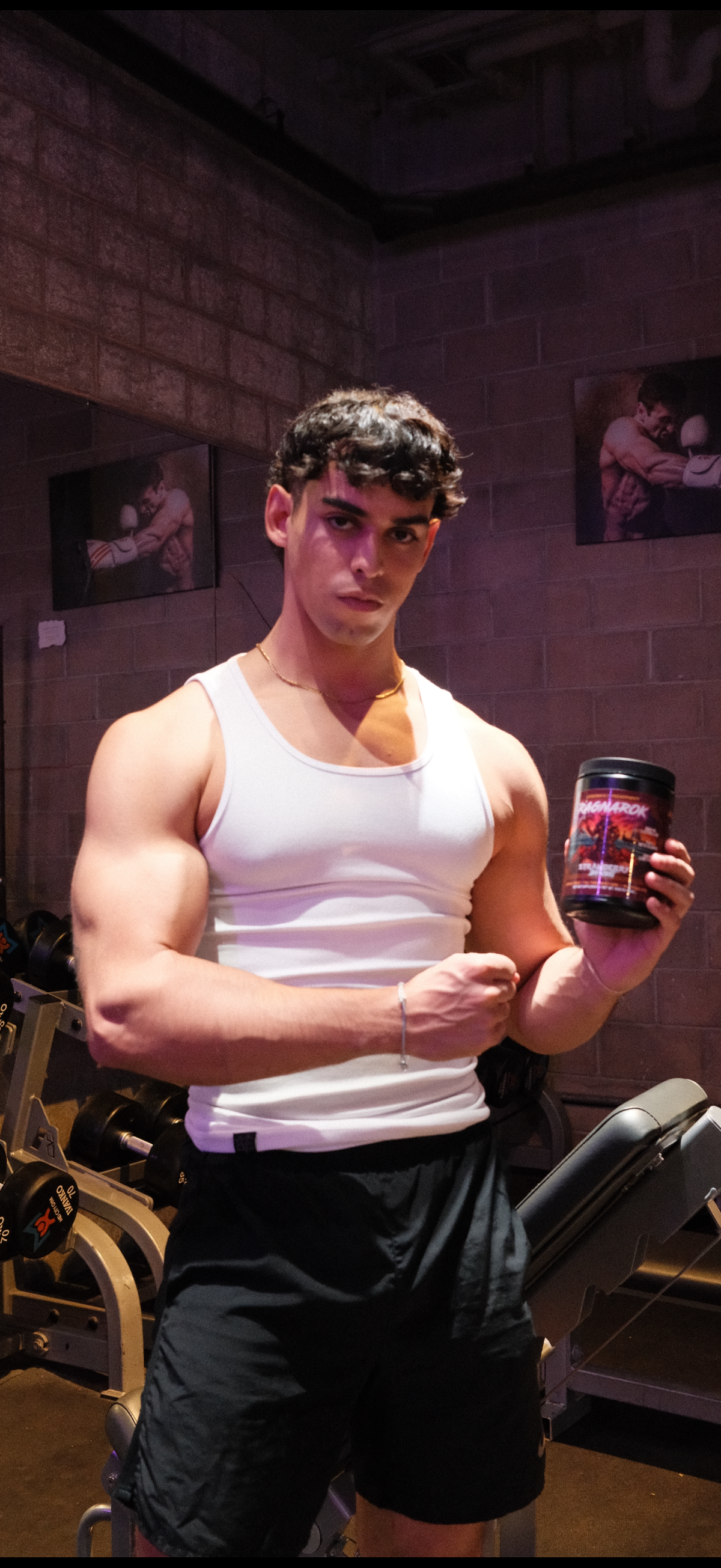 Man in a white tank top holding a tub of Ragnarok pre-workout